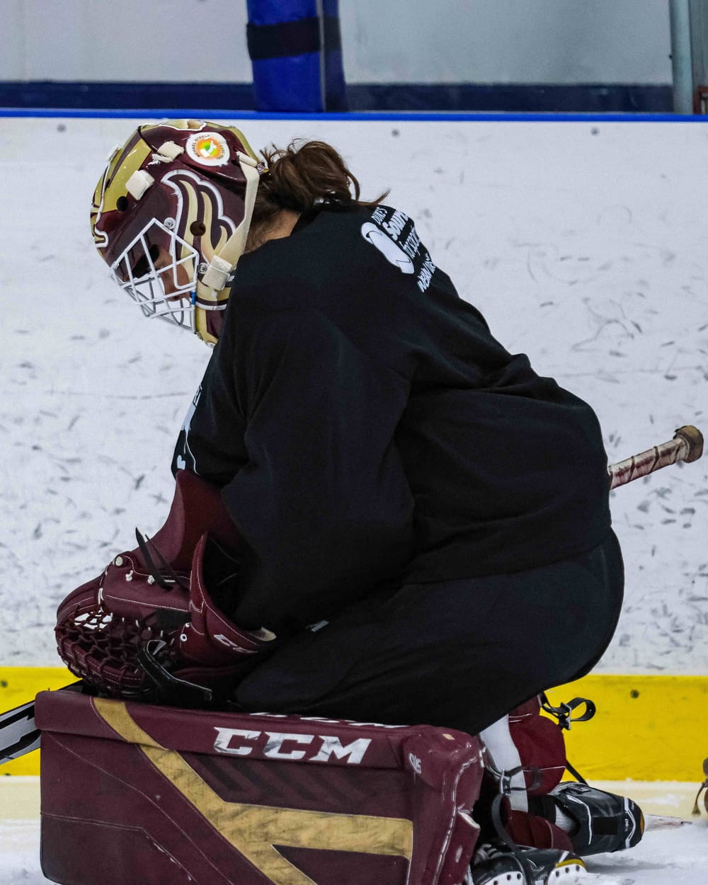 Kaitlyn Evelyn in her butterfly at practice, wearing a maroon and gold mask and CCM pads